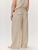 Pantalón sastrero de corte ancho, color beige con rayas verticales blancas y detalles de costuras pespunteadas.