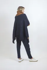 Poncho de tejido de punto en color azul marino con cuello alto y mangas en color ocre, con terminaciones de flecos en el ruedo.