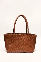 Bolso tipo tote de cuero vacuno, completamente trenzado a mano. El color es marrón oscuro, casi chocolate. Posee dos asas de hombro trenzadas.