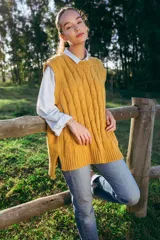 Chaleco mostaza de lana merino con tejido trenzado, corte oversized y largo asimétrico.