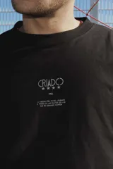 Remera negra de corte oversize con estampa frontal en color gris desgastado que hace referencia a la historia de la selección uruguaya. Presenta mangas largas integradas con diseño de rayas horizontales en tonos blanco, marrón y negro.