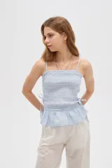 Top de algodón con diseño estampado de cuadros vichy en tonos celeste y blanco, corte al cuerpo con escote recto y tirantes finos. Presenta cuerpo fruncido tipo smock con cordones ajustables en los laterales que forman un pequeño volado en el ruedo.
