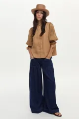 Blusa color tostado confeccionada en lino, con mangas abullonadas de ramie y detalles de bordado en punto smock en los puños.