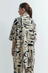 Vestido plisado color beige con estampado abstracto en negro, corte recto, cuello camisero y mangas cortas.