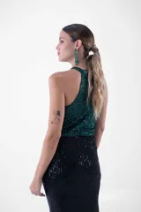 Vestido largo de fiesta con lentejuelas, compuesto por un top verde esmeralda con cuello halter y una falda negra ajustada con abertura lateral.
