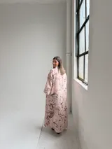 Vestido largo rosado con estampado floral en tonos marrones y beige, cuello drapeado y mangas largas holgadas.