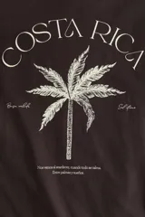 Remera de manga larga oversize confeccionada en punto de algodón suave, color marrón oscuro, con cuello redondo ribeteado, hombros caídos y pequeño estampado tipográfico en el pecho.