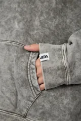 Buzo canguro oversize de algodón friza con efecto de teñido artesanal desgastado. Presenta capucha con cordones negros, bolsillo frontal tipo canguro y estampa pequeña de Popeye en el pecho.