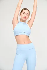 Top deportivo celeste con cuello alto y espalda deportiva con ribete blanco.