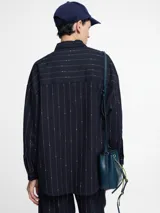 Camisa azul marino con botones en la parte delantera y bolsillo en el pecho. Diseño de rayas verticales bordadas con hilo metálico.