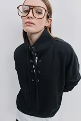 Buzo de algodón negro con calce relajado, cuello alto con cordones cruzados y ojales metálicos, bolsillos laterales y puños y ruedo elásticos.