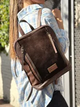 Mochila color chocolate combinada en cuero y gamuza, con cierre principal y bolsillos frontales con cierres verticales. Cuenta con asa superior y correas ajustables.
