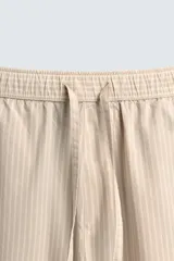 Pantalón relaxed fit color beige con rayas verticales finas, confeccionado en tejido de algodón. Cuenta con cintura elástica ajustable con cordón, bolsillos frontales y bolsillos traseros de plastrón.