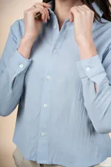 Camisa de algodón color celeste, con cuello camisero, manga larga, cierre frontal con botones y corte a la cintura.