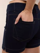 Short de jean azul oscuro de tiro alto y calce ajustado, con cintura ancha, cierre de cremallera y doble botón. Cuenta con bolsillos delanteros y dobladillo en las perneras.