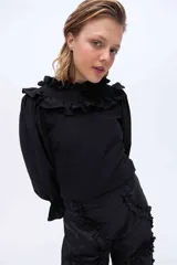 Blusa de manga larga color negro, con cuello alto fruncido y volados en el cuello y los hombros.