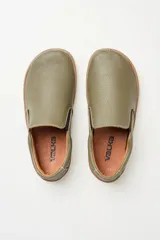 Zapatillas tipo slip-on de gamuza color beige, con diseño barefoot y suela de corcho texturizado. Presenta elásticos laterales negros para un calce fácil.