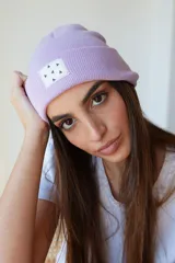 Gorro de lana color lila con etiqueta cuadrada blanca con diseño de triángulos negros.