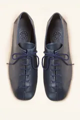 Zapato tipo oxford plano de cuero vacuno en color azul marino, con cordones al tono y suela de cuero.