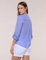 Blusa violeta de corte fluido, con cuello mao, escote en V y bolsillo plaqué en el pecho. Presenta mangas largas regulables con presilla y un lazo frontal para anudar en la cintura.