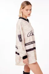 Camiseta oversize de poliéster color crema con diseño a cuadros, cuello en V con ribete negro, mangas largas con puños negros, logo "Blkmba" en el pecho y escudo "Mamba Soccer" en la manga.