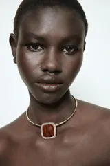 Collar tipo choker rígido de metal dorado con dije central cuadrado de resina marrón veteada, enmarcado por una hilera de cristales brillantes.