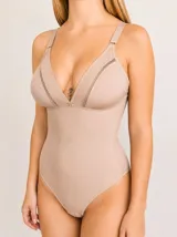 Body modelador y reductor de color beige, confeccionado en lycra. Presenta un diseño con escote en V profundo, detalles de encaje en los bordes del busto, breteles regulables y cierre con broches en la entrepierna.