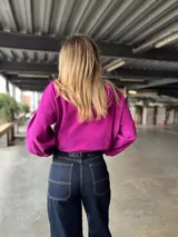 Pantalón de jean ancho, tiro alto, color azul oscuro, con pespuntes contrastantes en color claro. El ruedo está doblado mostrando el revés de la tela en tono gris claro.