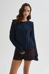 Blusa blanca de viscosa con cuello a la base, mangas largas abullonadas con puños ajustados, detalles de volados, encaje y botones frontales.