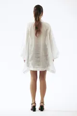 Camisa de lino blanca con corte oversize, cuello camisero y mangas amplias tipo kimono. Presenta detalles de costuras decorativas en el frente y cierre frontal con botones.