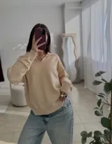 Sweater de punto color negro, con cuello polo y escote en V, de manga larga y diseño holgado con puños y ruedo acanalados.