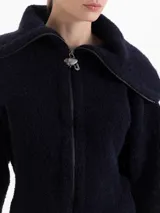Cardigan de tejido tipo corderito en color azul marino, con cuello alto, cierre frontal con tirador metálico en forma de fresa y mangas largas.