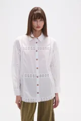Camisa de algodón blanca, de corte ancho, con botones de madera y detalles de encaje calado en el frente, mangas y ruedo. Tiene cuello camisero y manga larga.
