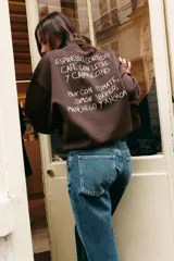 Sudadera de cuello redondo y manga larga con hombro caído, confeccionada en mezcla de algodón. Presenta un diseño liso en color marrón oscuro con un pequeño estampado gráfico a contraste en el pecho y detalle en el puño.