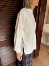 Sweater de punto acanalado en color natural, con cuello redondo, mangas largas con puños ajustados y diseño holgado con aberturas laterales en el ruedo.