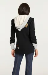 Blazer negro con capucha gris, solapas con muescas, cierre con botones y bolsillos con solapa en la parte delantera. Decorado con parches bordados de corazones, estrellas y otros motivos.