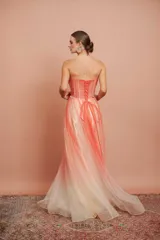Vestido largo de fiesta, strapless, con busto drapeado y falda de tul con degradé de color coral a blanco. Presenta bordados florales en el corpiño.