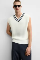 Chaleco de punto color crema con cuello en pico y ribete azul marino. Sin mangas y corte relajado.