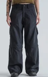 Pantalón cargo desmontable color negro, confeccionado en microfibra pesada con acabado satinado. Presenta diseño de seis bolsillos, cierre frontal con botón y cremallera, y estructura convertible que permite transformarlo en bermuda.