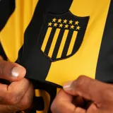Camiseta de fútbol Puma del Club Atlético Peñarol, modelo Home temporada 2026. Diseño a rayas verticales amarillas y negras, con cuello redondo negro y detalles amarillos en las mangas. Incluye logo Puma, escudo del club y sponsor Antel en el frente.