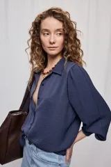 Camisa de manga larga color beige con cuello clásico y botonadura frontal. Presenta mangas con volumen sutil, puños abotonados y una silueta amplia de caída fluida.