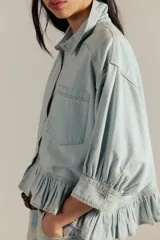 Camisa de denim de corte oversize, color celeste, con bolsillos frontales, mangas abullonadas y detalle de volados en el ruedo.