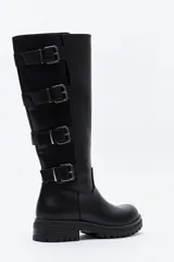 Bota de caña alta tipo biker en símil cuero color marrón oscuro. Presenta múltiples tiras horizontales con hebillas metálicas laterales y una suela robusta con relieve.