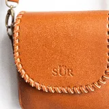 Mini cartera bandolera de cuero, de formato compacto y diseño atemporal con solapa frontal y costuras artesanales decorativas en el borde. Cuenta con el logotipo de la marca grabado en la parte delantera y correa larga regulable.