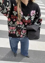 Buzo tejido de algodón negro con diseño jacquard de flores multicolor, cuello en V y mangas largas.
