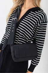 Bolso de hombro acolchado color negro, con diseño de cuadrícula. Posee una correa ancha y ajustable con hebilla metálica plateada. El cuerpo del bolso es rectangular con solapa frontal.