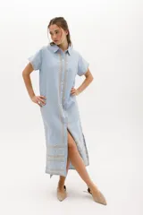 Vestido camisero de lino color lila con bordados rojos en contraste. Presenta un diseño de largo midi con cuello camisero, cierre frontal de botones y mangas cortas. Los detalles bordados recorren la botonadura, los puños y el ruedo de la prenda.