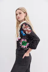 Saco corto de lentejuelas negras con bordados florales multicolores hechos a mano. Presenta cuello redondo, mangas largas y cierre frontal con ganchos invisibles.