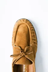 Mocasín de estilo relajado confeccionado en cuero gamuzado color tostado. Presenta detalles fruncidos en la puntera, cordones decorativos en el empeine y el logo de la marca grabado en el lateral.