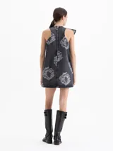 Vestido corto de denim con lavado gris y estampado floral en contraste. Presenta un diseño sin mangas con escote cerrado y un volado asimétrico en el frente que aporta movimiento. Posee un calce suelto y cierre en la espalda.